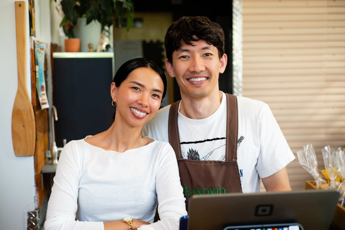 Two small business café owners standing behind the counter with a laptop, planning their EOFY equipment purchases