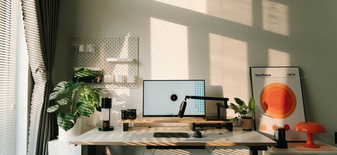 Sunlit home office desk with monitor, standing desk and plants, illustrating a working from home tax deduction in Australia