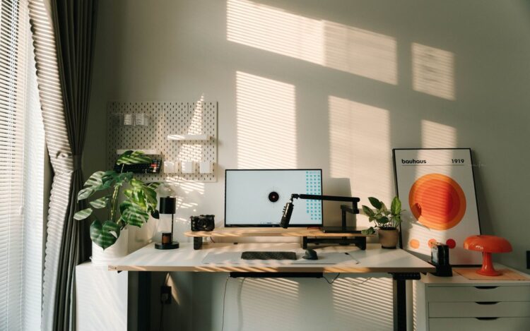 Sunlit home office desk with monitor, standing desk and plants, illustrating a working from home tax deduction in Australia